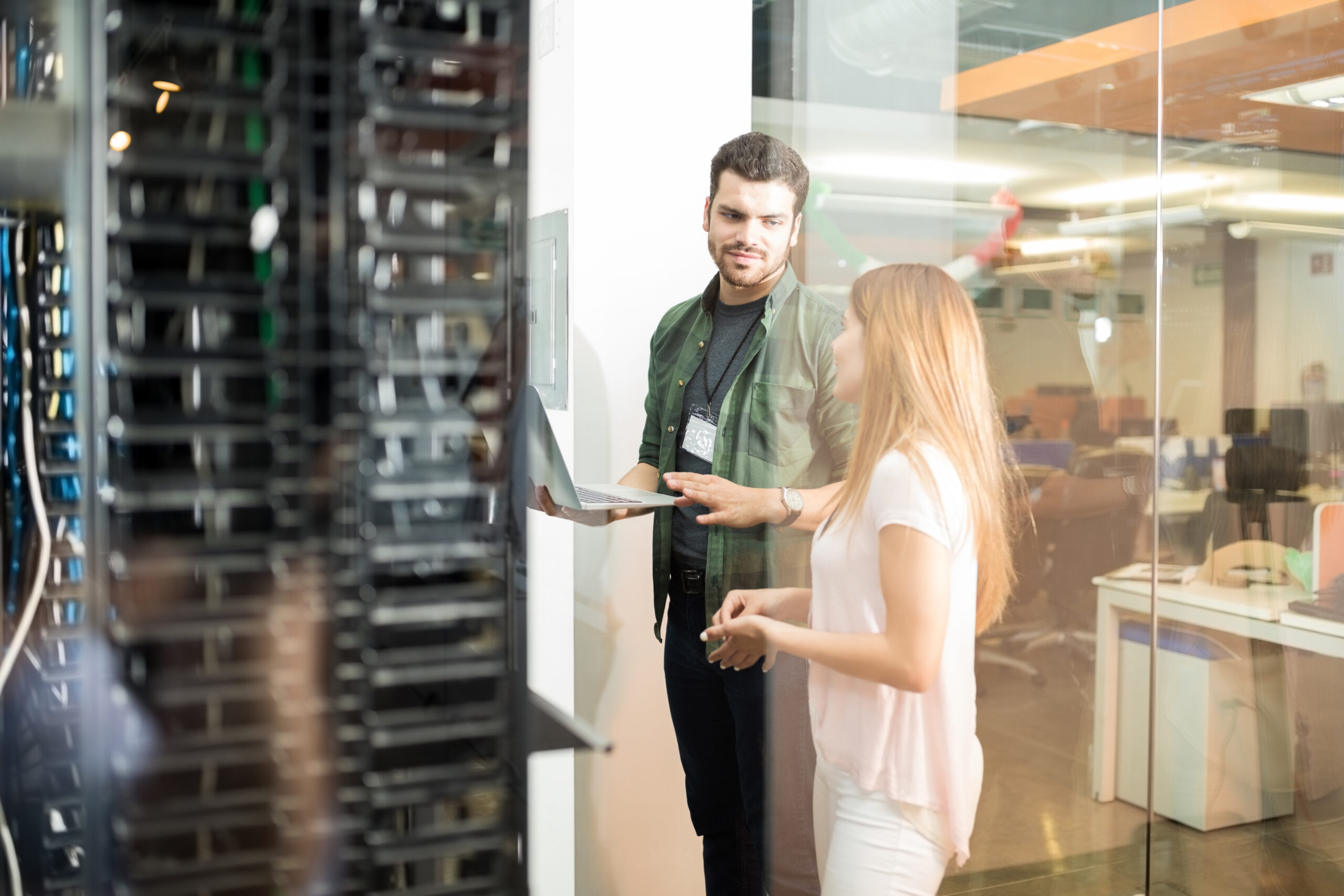 Colleagues discussing in office server room Two business people standing in server room with laptop and discussing